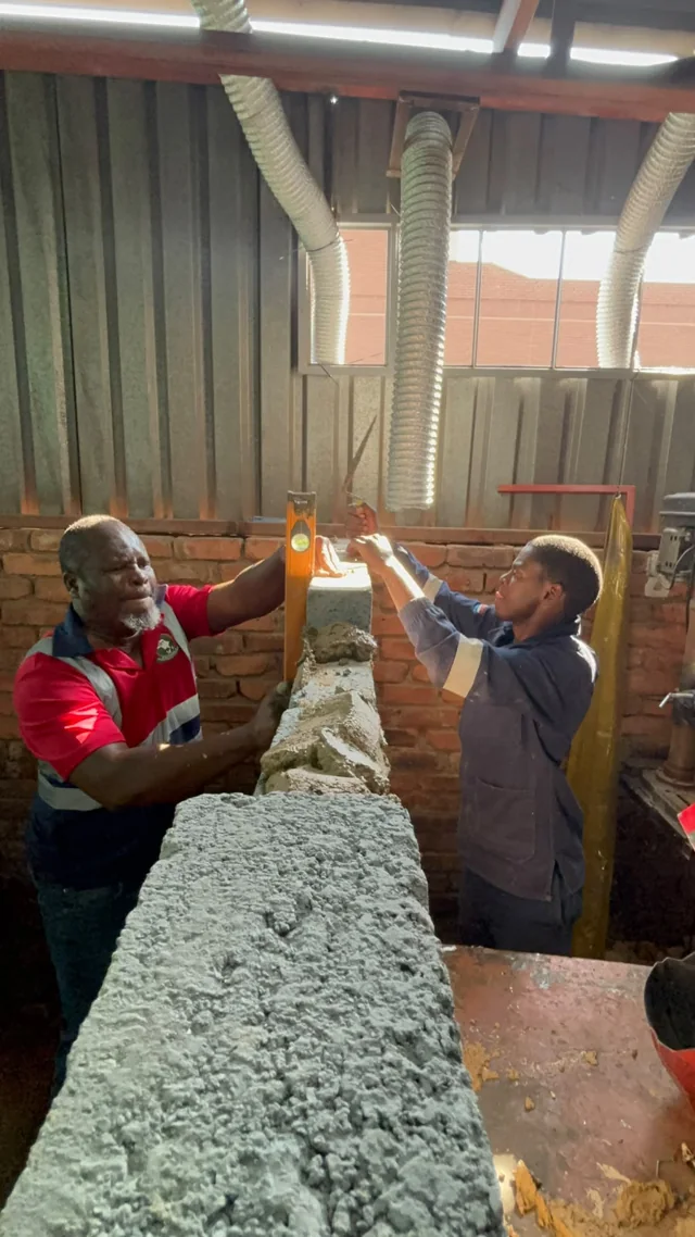Two participants beside a training wall during building practicals