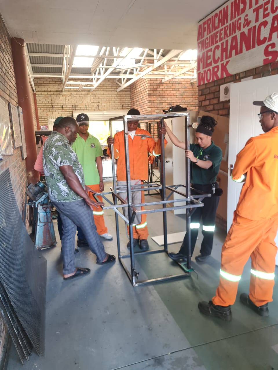 Mechanical students and facilitator standing around a steel frame project in a workshop