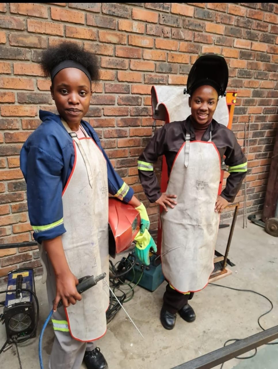 Two AIET students in aprons and protective gear during a welding practical